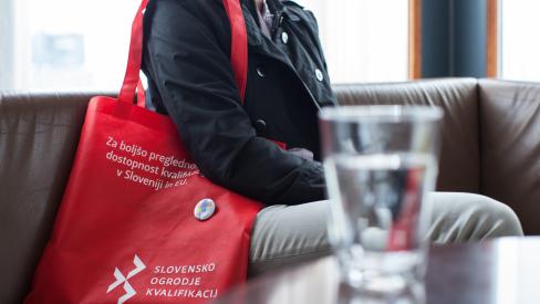 Woman sitting on a sofa with a red SQF promotional bag in front of a glass of water. 